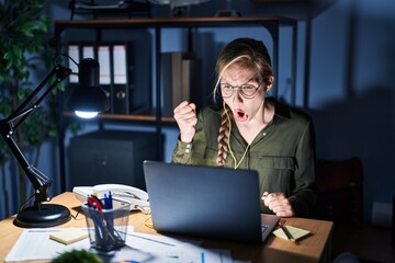 Sticker - Young blonde woman working at the office at night angry and mad raising fist frustrated and furious while shouting with anger. rage and aggressive concept.