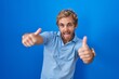 © Krakenimages.com - Caucasian man standing over blue background approving doing positive gesture with hand, thumbs up smiling and happy for success. winner gesture.