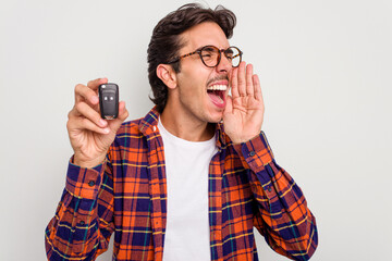 Wall Mural - Young hispanic man holding car keys isolated on white background shouting and holding palm near opened mouth.