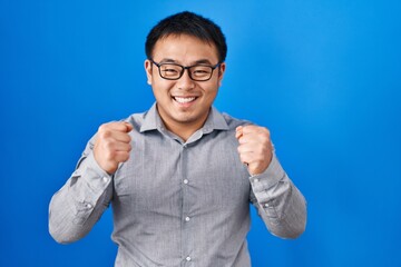 Sticker - Young chinese man standing over blue background celebrating surprised and amazed for success with arms raised and open eyes. winner concept.