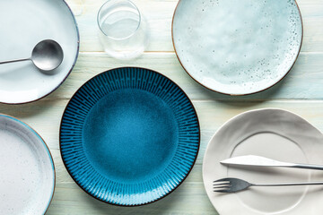 Modern tableware set with cutlery and a vibrant blue plate, with a glass, overhead flat lay shot. Trendy dinnerware on a rustic wooden background