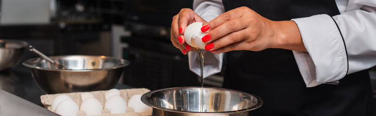 partial view of african american woman braking raw egg above bowl while cooking in kitchen, banner.