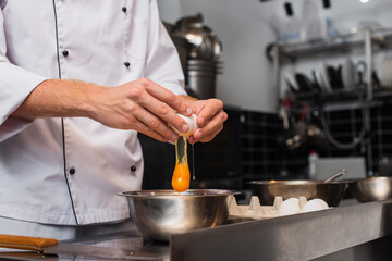 cropped view of man breaking raw egg above bowl while cooking in kitchen.