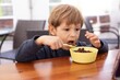 © Татьяна Волкова - Little boy sit on chair at table and with interest watch cartoon on tablet computer closeup. Kid of kindergarten age open mouth to eat chocolate balls with milk. Ready breakfast, gadget addiction