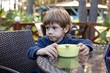 © Татьяна Волкова - Pretty little boy sit on chair at table in cafe on summer terrace and look away. Kid of kindergarten age having dinner outdoor in forest. Children food, health resort, vacation, nature