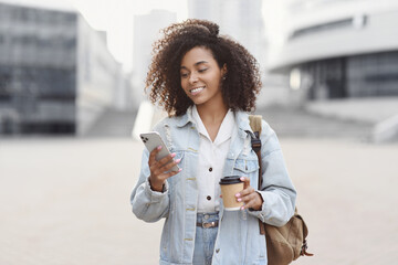 Wall Mural - Young beautiful woman using smartphone in city. Smiling student girl texting on her mobile phone. Coffee break. Modern lifestyle, connection, business concept