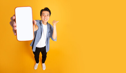 Wall Mural - image of asian man holding phone, isolated on yellow background
