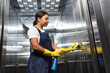 young bi-racial cleaner in workwear washing office elevator with sponge.