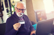 © Solid photos - Smiling senior man online shopping using credit card and laptop