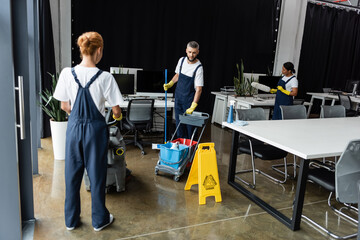 Wall Mural - woman in overalls with floor scrubber machine near man with cart of cleaning supplies.