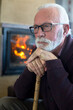 © Solid photos - Senior man sitting with walking cane by the fireplace in winter