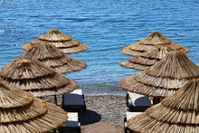 Empty Pebble Beach With Wicker Parasols And Lounge Chairs. Picturesque View To Sea With Blue Water, Summer Resort