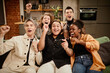 © Seventyfour - Group of young intercultural ecstatic friends shouting while sitting on couch in living room on weekend and playing video game