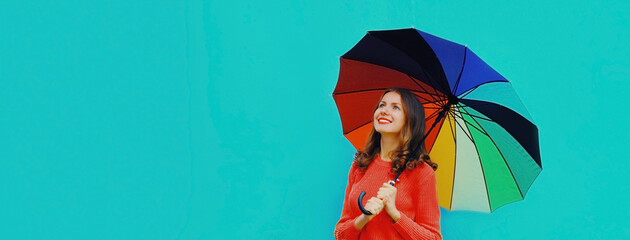 Autumn portrait of happy smiling young woman holding colorful umbrella wearing red knitted sweater on blue background