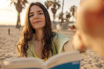 Poster - Attractive smiling dark-haired woman reach hand to camera and holding book. Staying on the palms background. Technology, lifestyle concept 