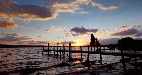 Wall Mural - Boy and Girl Looking at the lake, enjoying dramatic sunset and walking on old wooden pier, 4k video