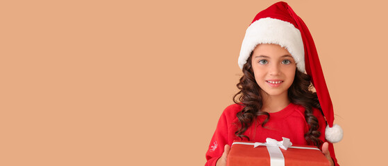 Wall Mural - Cute little girl in Santa hat and with Christmas gift on beige background with space for text