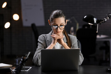 Beautiful businesswoman working with laptop in office at night