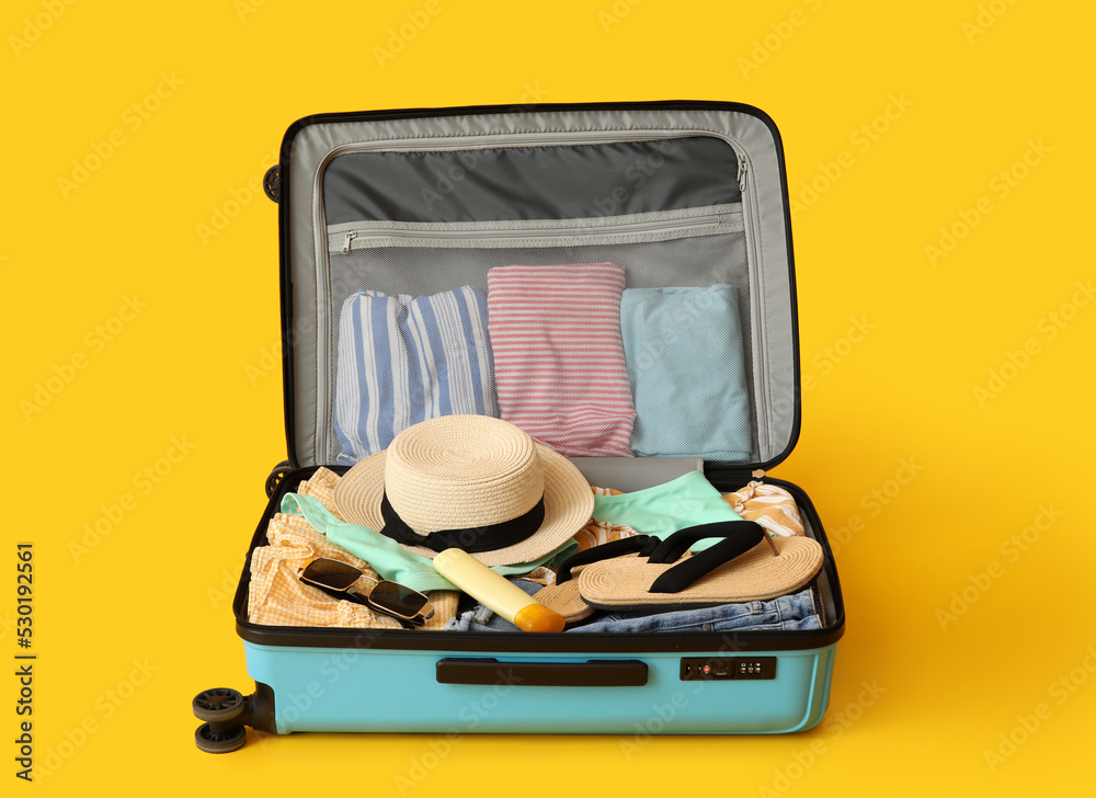 Open suitcase with beach accessories and clothes on color background