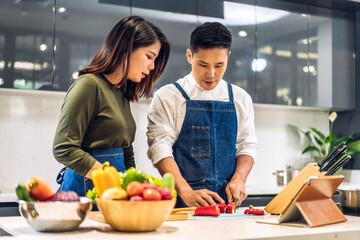 Wall Mural - Young asian family couple having fun cooking together with fresh vegetable healthy food clean on table.Happy couple prepare the food yummy eating lunch in kitchen