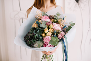 Wall Mural - Very nice young woman holding big and beautiful bouquet of fresh hydrangea, roses, eucalyptus, peonies in pink and green colors, cropped photo, bouquet close up