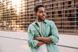 © Look! - Cool young african guy posing with his arms crossed in front of him standing on street. Brunette man wears green shirt in spring. Relaxed lifestyle, concept