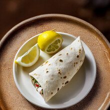 Hot Burrito On A White Ceramic Plate With Two Cut Lemon Pieces Near