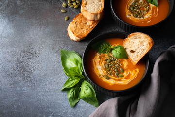 Pumpkin soup with bread, seeds and basil leaf on dark background