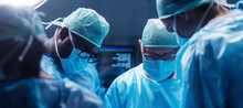 Diverse Team Of Professional Medical Surgeons Perform Surgery In The Operating Room Using High-tech Equipment. Doctors Work To Save A Patient In A Modern Hospital. Medicine, Technology And Healthcare.