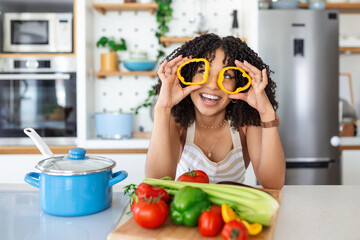 Wall Mural - Photo of young woman smiling while cooking salad with fresh vegetables in kitchen interior at home