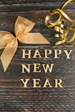Happy New Year Wooden Text Decorated With Golden Bow And Serpantine On Wooden Dark Background. Festive Greeting Card For New Year Holidays