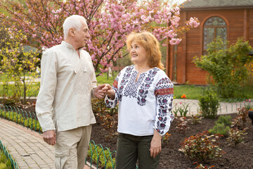 Wall Mural - mature couple wearing Ukrainian embroidered shirt relaxing in park in spring or summer near sakura blooming tree