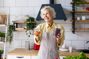 Wall Mural - beautiful elderly gray haired senior woman cook in cozy kitchen with fresh organic vegetables, tomatoes, cabbage, lettuce, cucumbers on table cooking healthy vegetable salad, healthy food active life