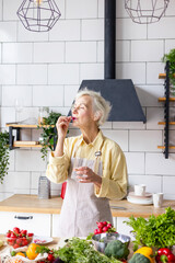 Wall Mural - beautiful elderly grey haired senior woman in cozy kitchen takes vitamin supplement in capsule, drinks pure water from glass, biologically active food additives for full life, healthy food active life