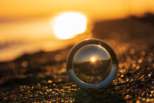 Glass Lens Globe On Sandy Beach On Sea Surf And Blue Sky Background At Sunset.