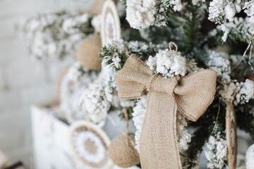 Wall Mural - Beautiful Christmas tree decorated with synthetic snow and burlap bow in living room with white brick wall. Merry Christmas, New Year and Happy Holidays background. Eco festive style