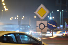 Roundabout Road Signs With Blurred Cars On City Street Traffic At Night. Urban Transportation Concept