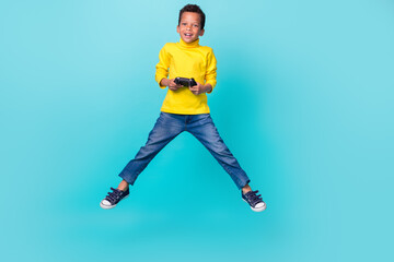 Poster - Full length portrait of excited carefree boy jumping arms hold controller isolated on teal color background