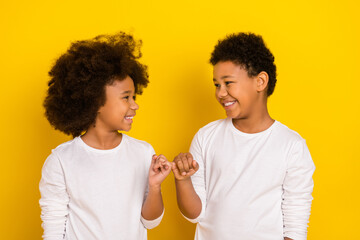 Wall Mural - Photo of sweet friendly schoolboy schoolgirl wear white shirts holding small fingers isolated yellow color background