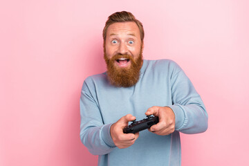 Wall Mural - Portrait of handsome guy with red hairstyle wear blue long sleeve hold joystick playing excited game isolated on pink color background