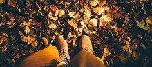 Autumn Leaves On The Ground, Top View Of A Woman's Feet In Boots Standing On Autumn Leaves.