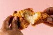 Image of hands of african american man tearing croissants on pink background