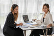 © ArLawKa - A team of Asian businesswomen discussing something and smiling as they sit at a desk in the office of women working together analyzing finances.