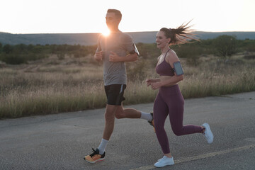 healthy young couple jogging in the city streets in the early morning with a beautiful sunrise in the background. 