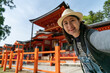 © PR Image Factory - happy Asian Japanese female visitor taking self portrait with Kasuga grand shrine in nara japan. she smiles at camera with the red temple building at background