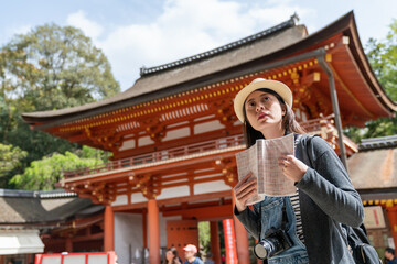 Wall Mural - confused Asian Korean girl visitor holding travel book and looking into distance while wondering what to see first at Kasuga Taisha shinto shrine in nara japan