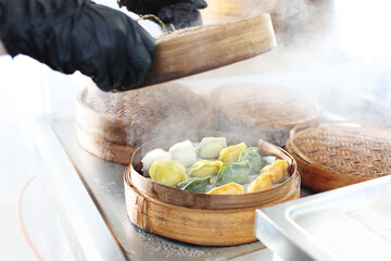 Cooking colorful dumplings in a bamboo steamer baskets. Making traditional dim sum, Chinese dumplings on steam.