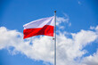 Polska flaga biało-czerwona powiewająca na maszcie na tle błękitnego nieba