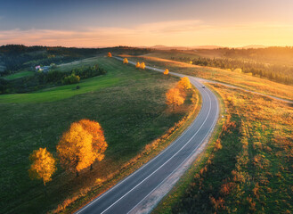 Wall Mural - aerial view of road, hills, green meadows and colorful trees at sunset in autumn. top view of mounta