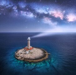 Wall Mural - lighthouse on smal island in the sea and milky way at night in summer. aerial view of beautiful ligh
